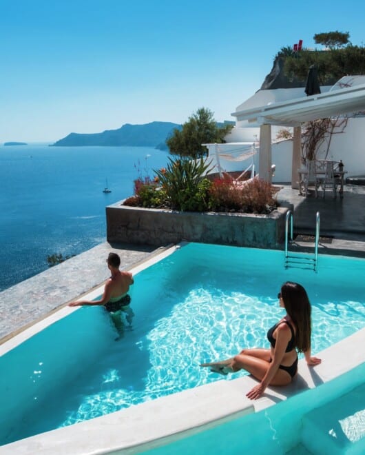 Guestσ at the edge of the infinity pool and volcano view from the terrace of one of Andronis three Santorini adults-only hotels in Oia